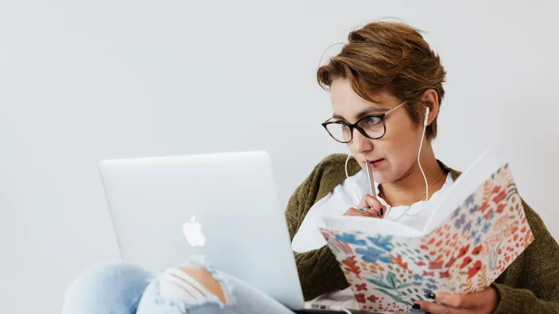 Femme à lunettes qui prend des notes dans un carnet devant son ordinateur portable