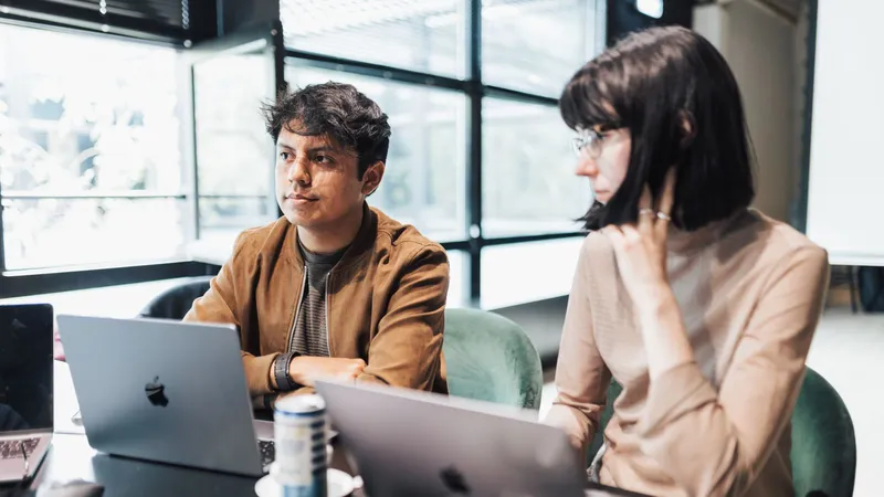 Deux jeunes professionnels assis à une table de réunion, devant leurs ordinateurs portables