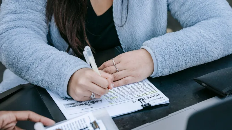 Une étudiante remplit un document posé sur un porte-bloc, à une table de travail