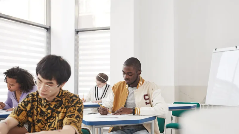 Étudiants composant à une épreuve écrite, assis à des tables individuelles dans une salle claire