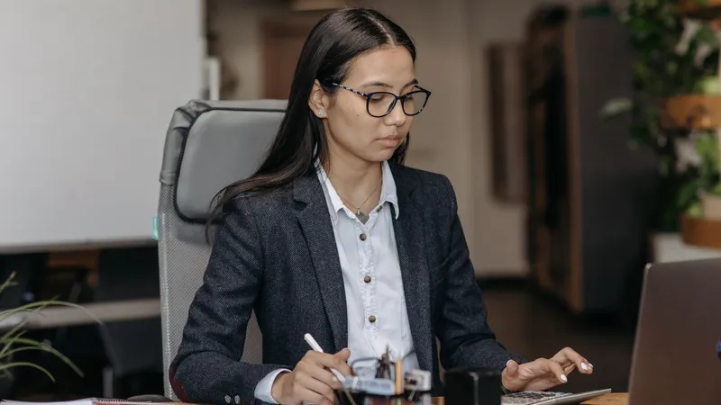 Jeune femme en veste de tailleur travaillant à son bureau, devant un ordinateur portable et une calculatrice