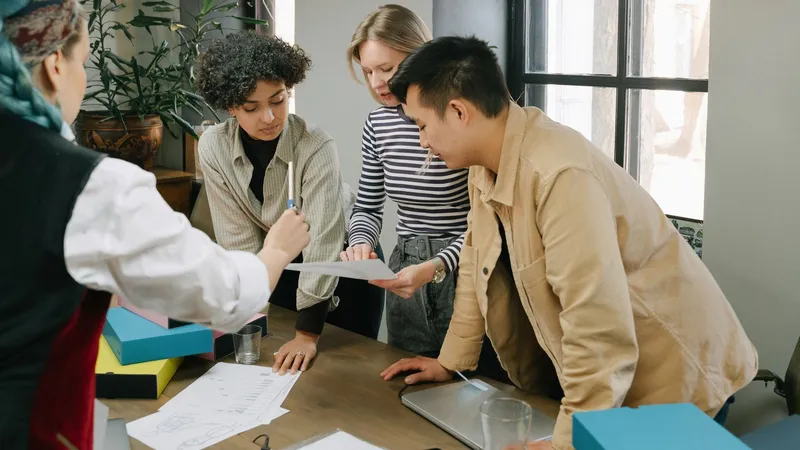 Quatre jeunes professionnels penchés sur des documents autour d’une table de réunion, dans un bureau lumineux
