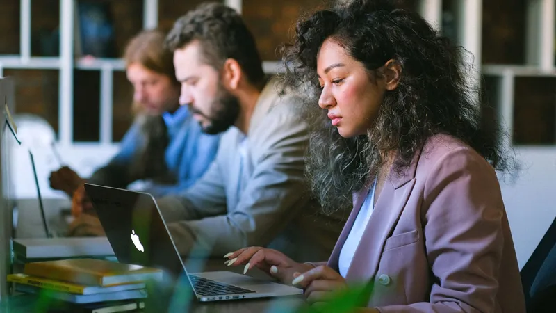 Trois jeunes salariés concentrés sur leurs ordinateurs portables dans un bureau partagé