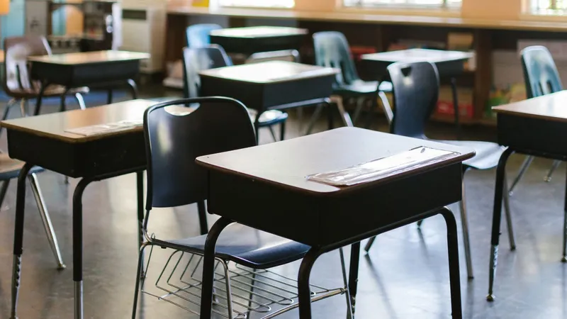 Salle de classe vide, avec des tables individuelles et des chaises alignées devant de grandes fenêtres