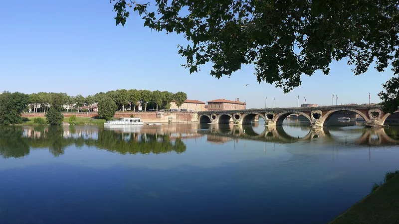 Le Pont-Neuf de Toulouse et ses arches de brique se reflètent dans la Garonne, sous un ciel bleu